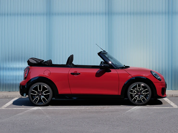 側面視角Chili Red車色的MINI Cooper敞篷車停靠在街道上。
